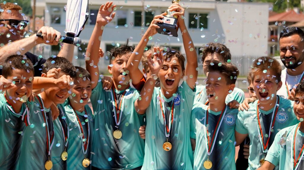 Group of boys celebrating a soccer tournament victory with confetti and trophy.