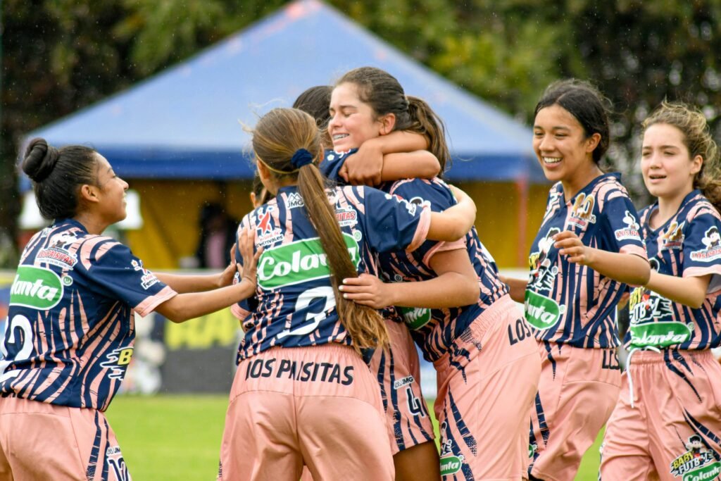 Teenage girls' soccer team celebrating a victory on the field outdoors.