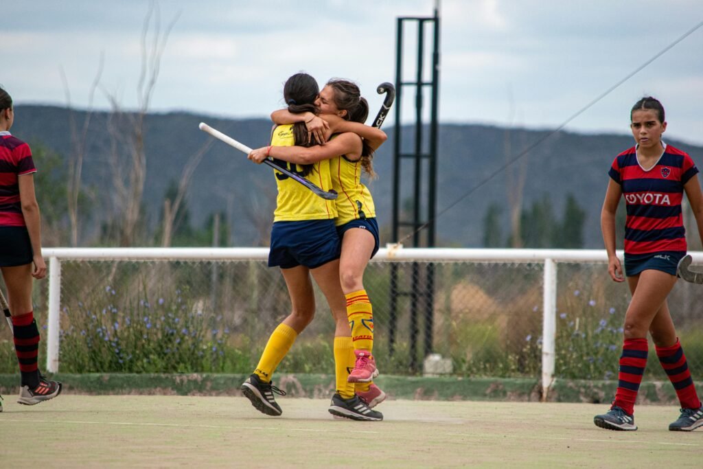 Two young female field hockey players celebrate on a sunny day outdoors.