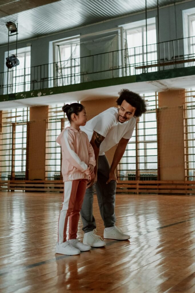 Father and daughter smiling together in a gymnasium on a basketball court.